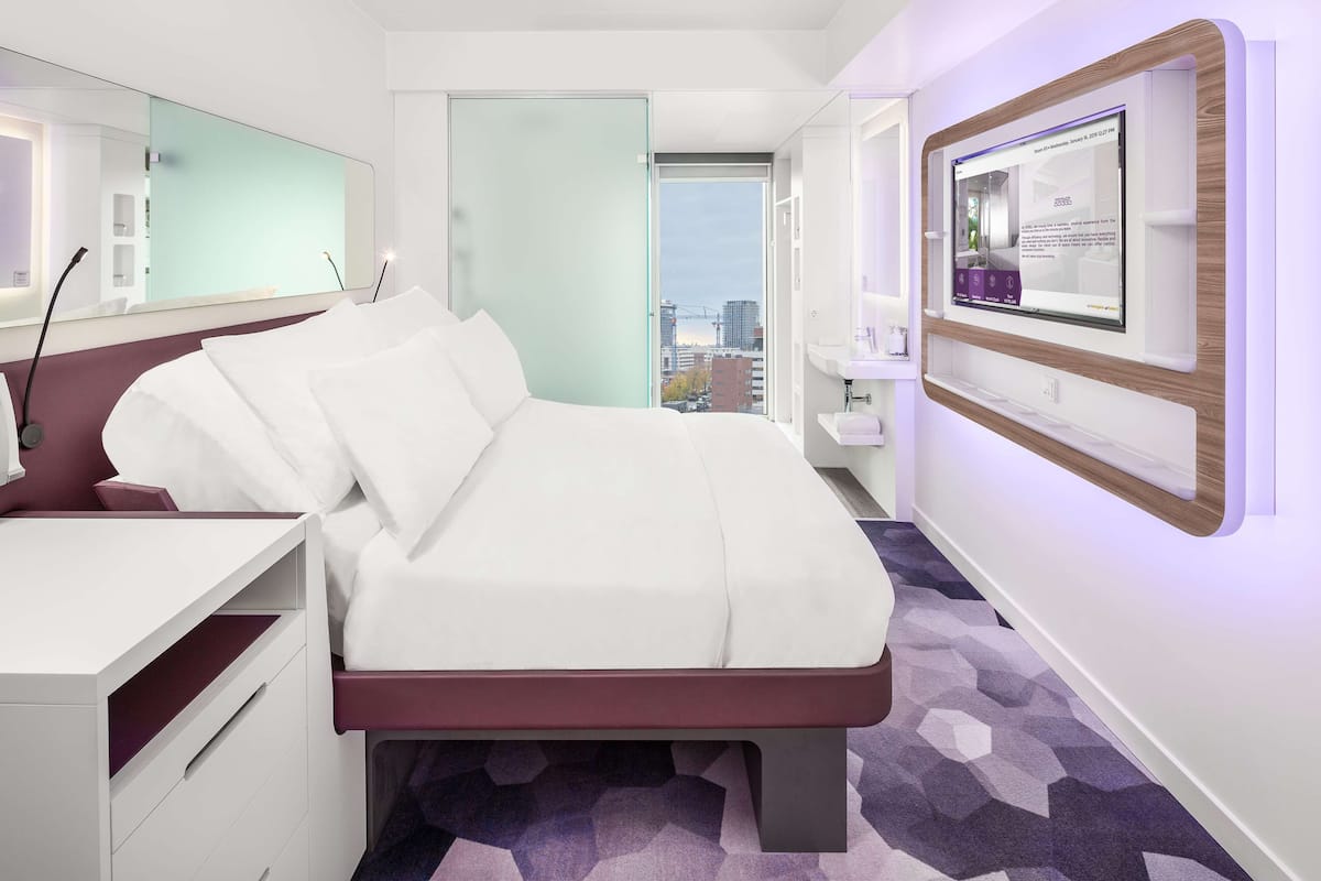 Une chambre d’hôtel moderne, dotée d’un grand lit, d’un bureau, d’un miroir et d’un téléviseur fixé au mur.