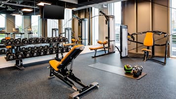 Un gimnasio con diversos equipos de ejercicio, incluyendo mancuernas, bancos y una máquina de poleas.