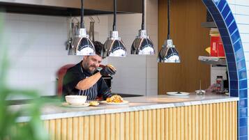 Una encimera de cocina con un chef preparando comida, luces colgantes en la cocina y un salpicadero de azulejos.