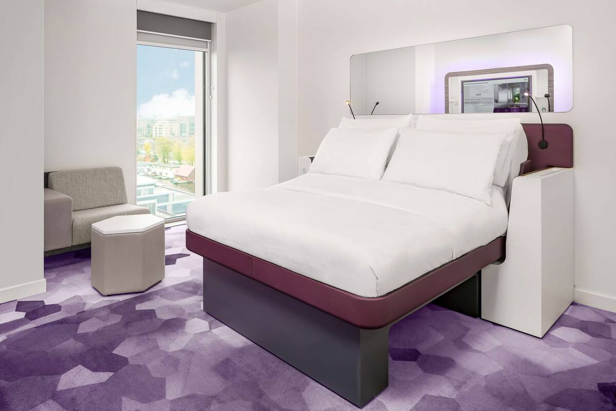 Une chambre d’hôtel moderne dotée d’un grand lit, d’un petit canapé, d’une table de chevet et d’une grande fenêtre donnant sur la ville.