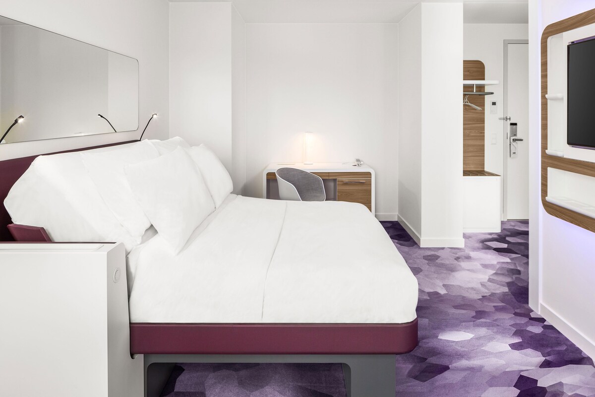 Una habitación de hotel con una cama, un escritorio, una silla, una lámpara y un televisor.