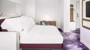 A hotel room with a bed, a desk, a chair, a lamp, and a television.