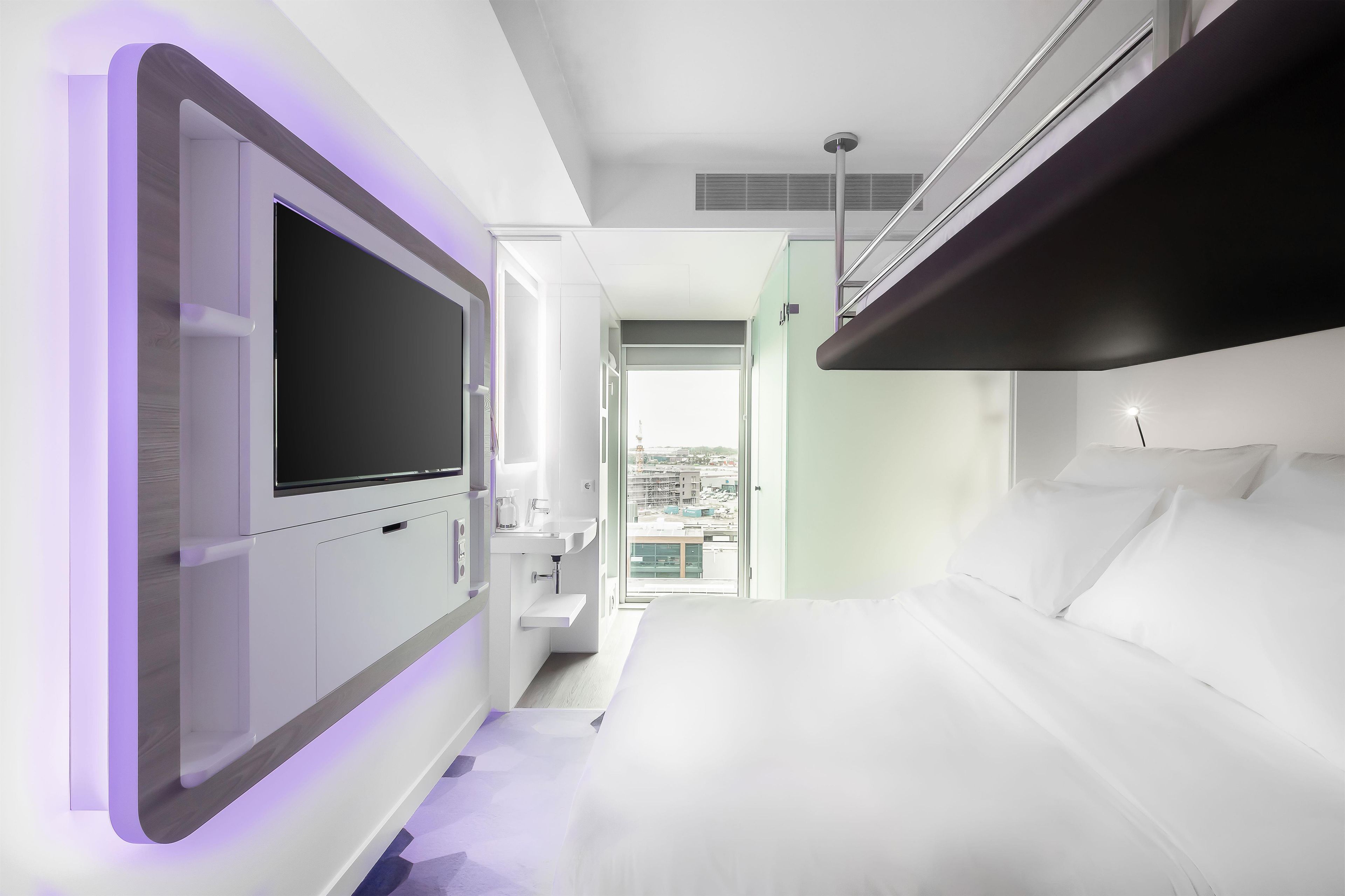 Habitación de hotel moderna con una cama grande, televisión de pantalla plana, lavamanos integrado y balcón con vista a la ciudad.