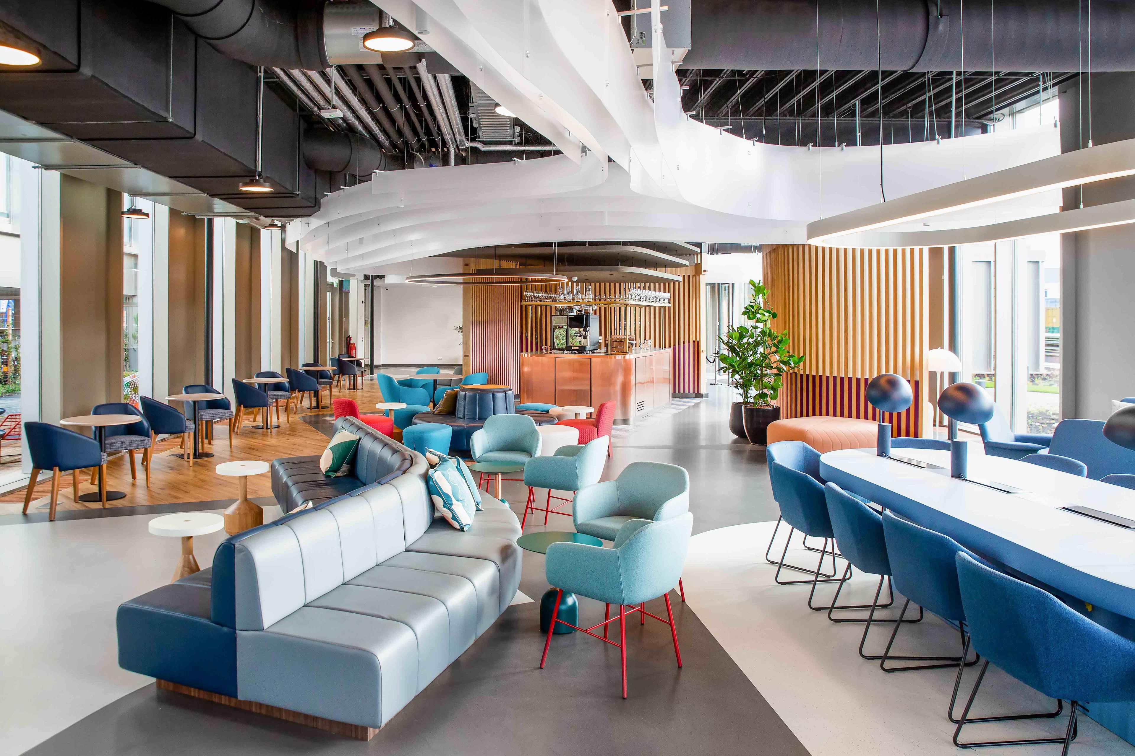 A modern lounge area with seating arrangements, a bar, and a large window providing natural light.