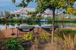 A wooden deck with outdoor seating and a view of a calm water body. - YOTEL Amsterdam (Amsterdam)