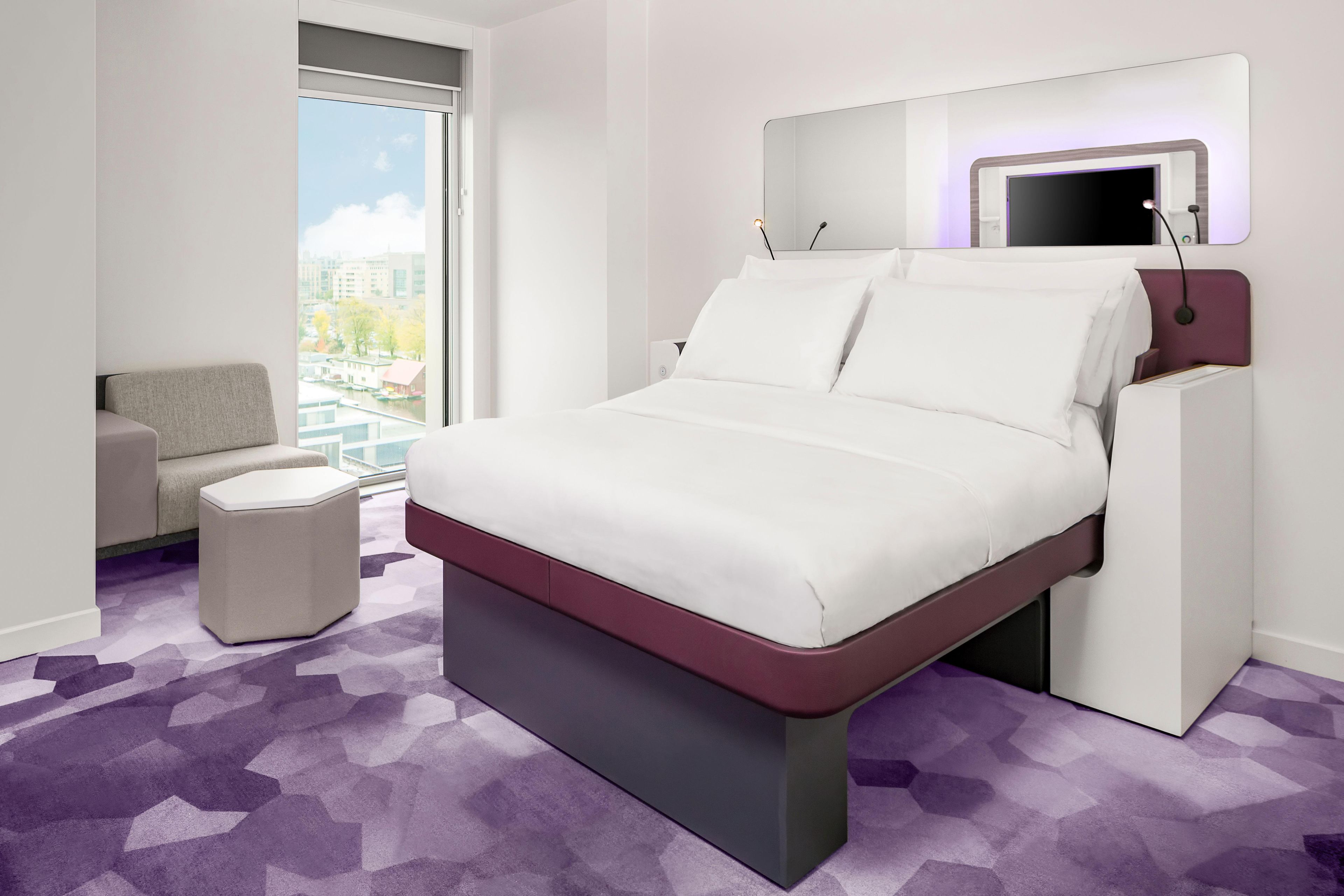 Una habitación de hotel moderna con una cama grande, una zona de estar y vistas a la ciudad.