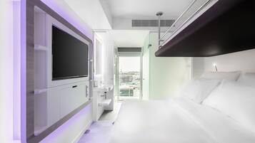 A modern hotel room with a large bed, a flat-screen TV, a built-in sink, and a balcony with a city view.