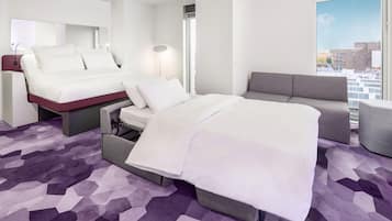 Habitación de hotel con cama, sofá, escritorio y ventana grande con vista a la ciudad.