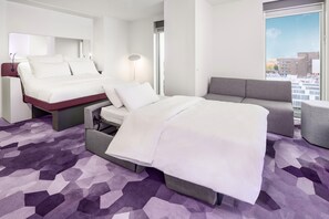 A hotel room with a bed, a sofa, a desk, and a large window with a city view. - YOTEL Amsterdam (Amsterdam)