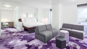 A modern hotel room with a bed, grey sofa, armchair, and a desk with a chair. - YOTEL Amsterdam (Amsterdam)