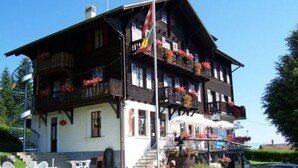 Un edificio de estilo chalete tradicional con balcones, una bandera y asientos al aire libre.