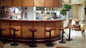 Un restaurante con barra de madera, taburetes y una zona de estar con mesas y sillas.