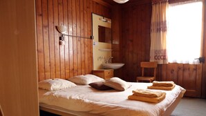 Un dormitorio con paneles de madera, una cama, una mesita de noche, un espejo y una ventana con cortinas.