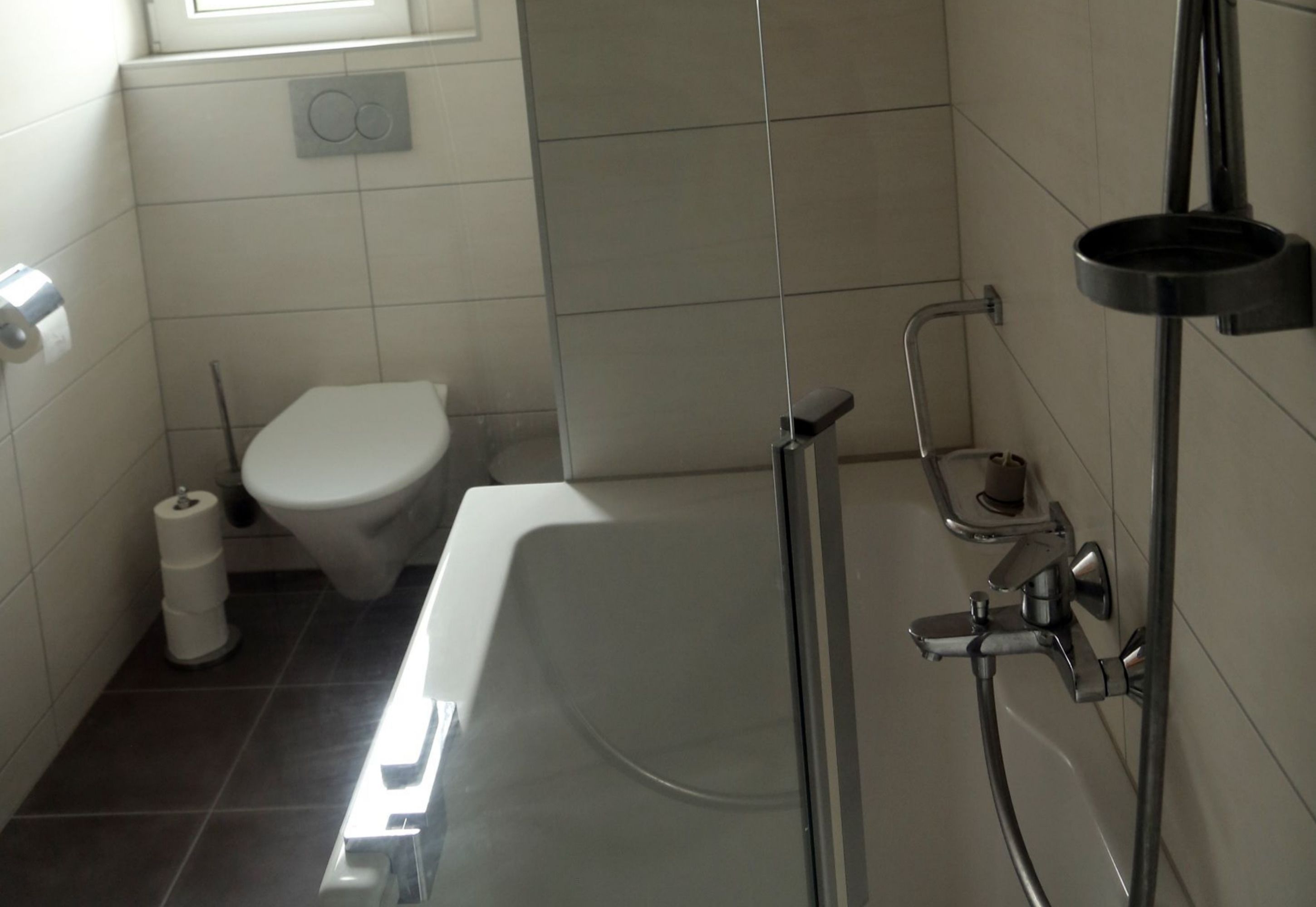 Casa de banho moderna com sanita branca, cabine de duche com vidro e suporte para papel higiénico.