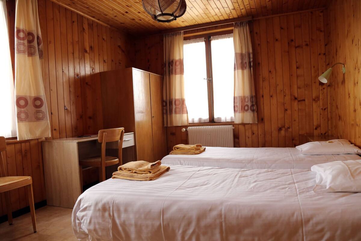 Una habitación de madera con dos camas, un escritorio, una silla y un radiador.