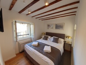 Un dormitorio con una cama grande, una ventana con vistas, un radiador y un techo con vigas a la vista.