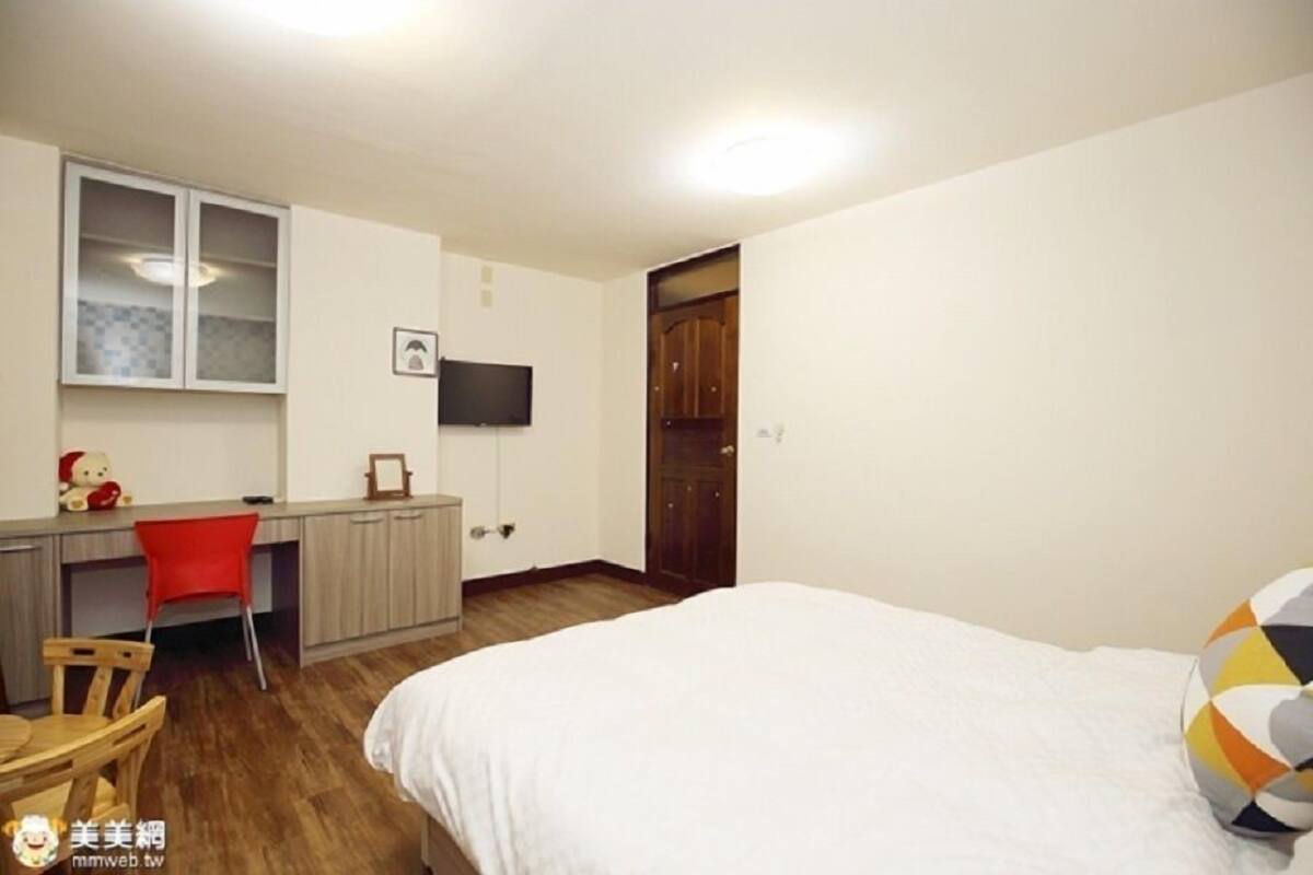 A bedroom with a bed, a desk, a chair, and a TV on the wall.