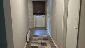 A narrow hallway with a patterned rug, white walls, and a door with a number. - 8 Seasons (Nesseby)