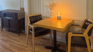A dining area with a wooden table, two chairs, a small potted plant, and a vintage radio. - 8 Seasons (Nesseby)