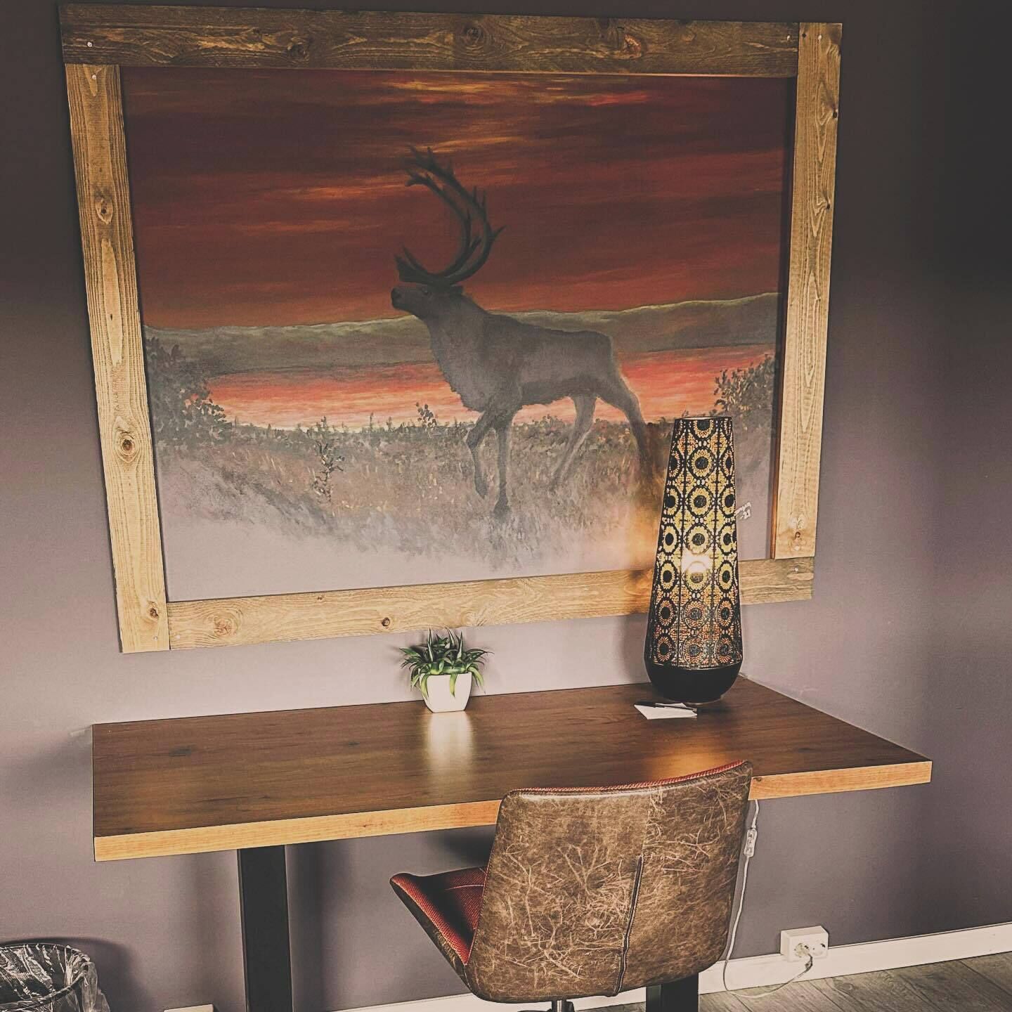 A framed painting of a deer on a hill, a vase, and a chair on a table.