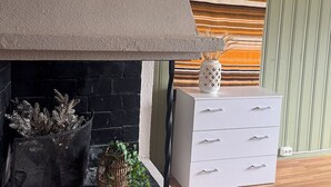A fireplace with a stone surround, a white cabinet with drawers, and a striped fabric draped over a window. - 8 Seasons (Nesseby)