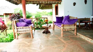A covered outdoor seating area with wicker furniture and stone flooring. - Fabio House (Diani Beach)