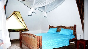 A bedroom with a bed, a small wooden stool, and a window with a curtain. - Fabio House (Diani Beach)