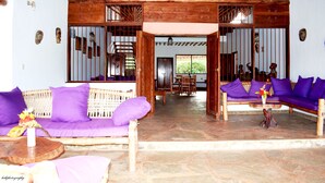 A room with a wooden ceiling, a stone floor, and purple sofas. - Fabio House (Diani Beach)