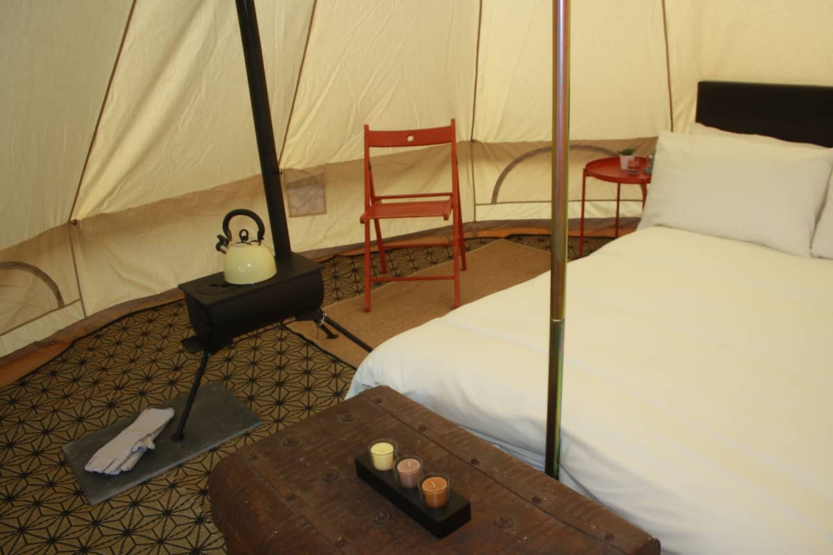 A tent with a bed, a chair, a table with candles, and a kettle.