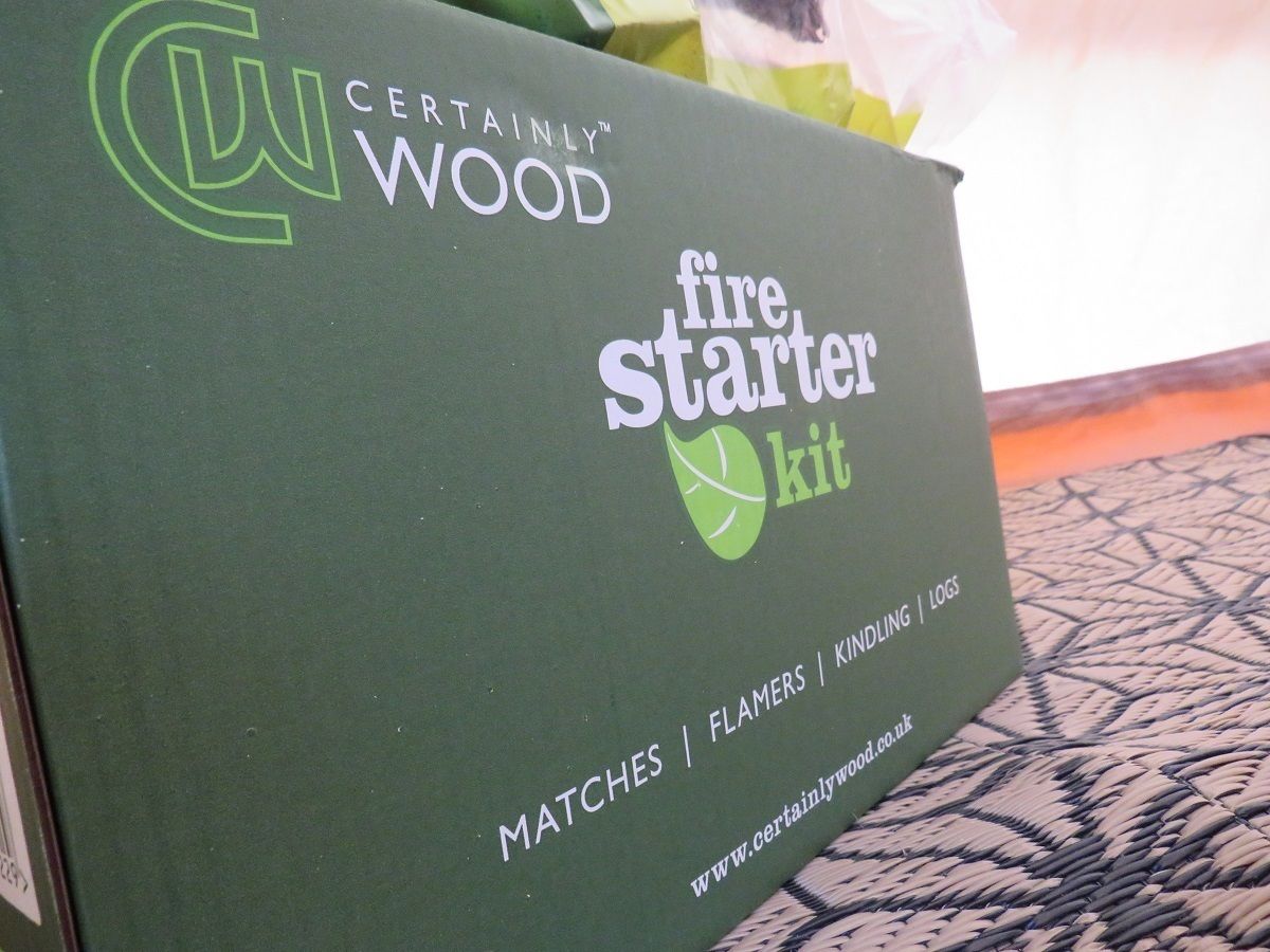 A green box labeled "CERTAINLY WOOD fire starter kit" with text indicating it contains matches, flammers, kindling, and logs.
