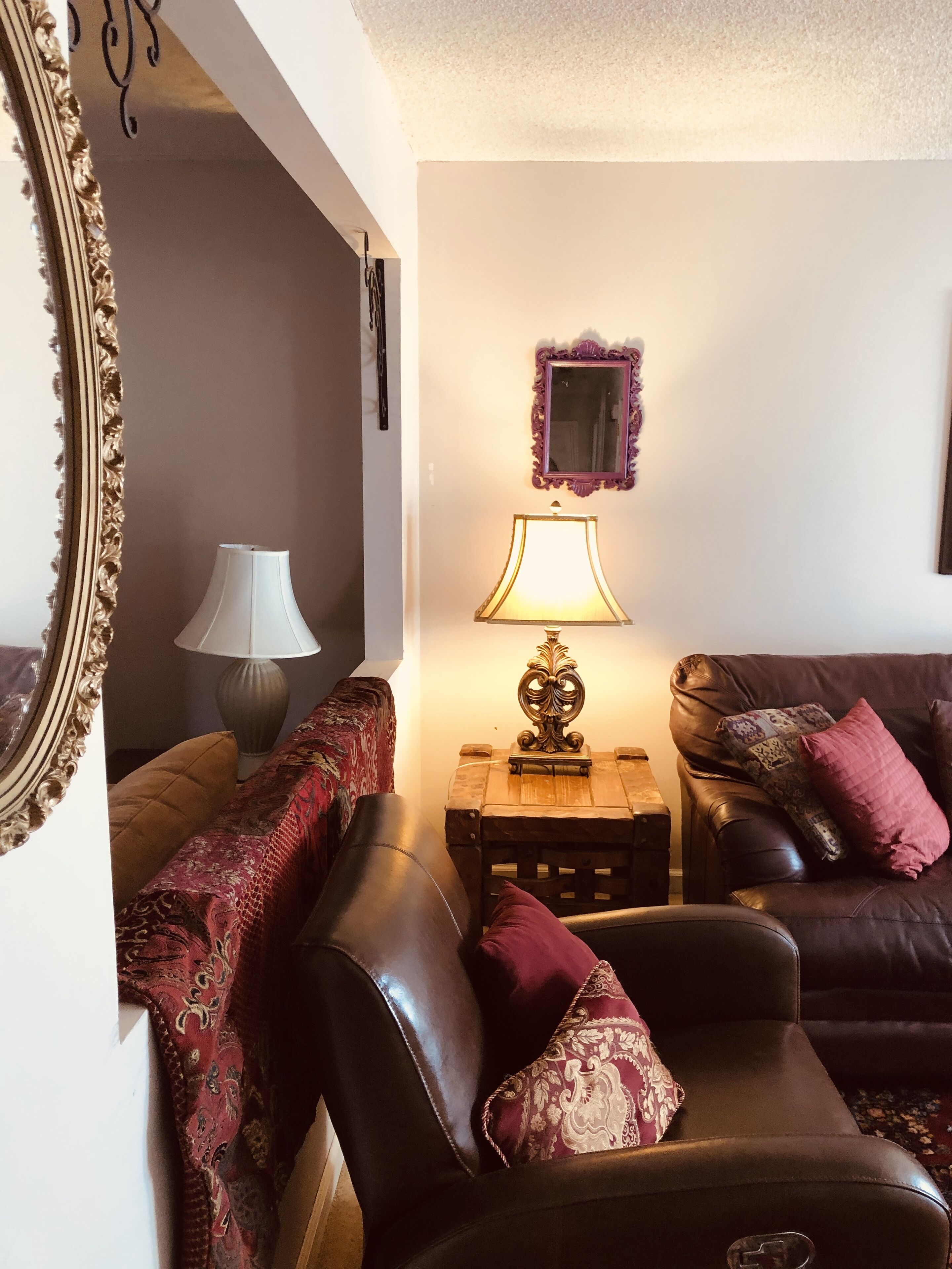 Un salon avec un canapé en cuir marron, un plaid à motifs, une lampe, un miroir et une petite table en bois.