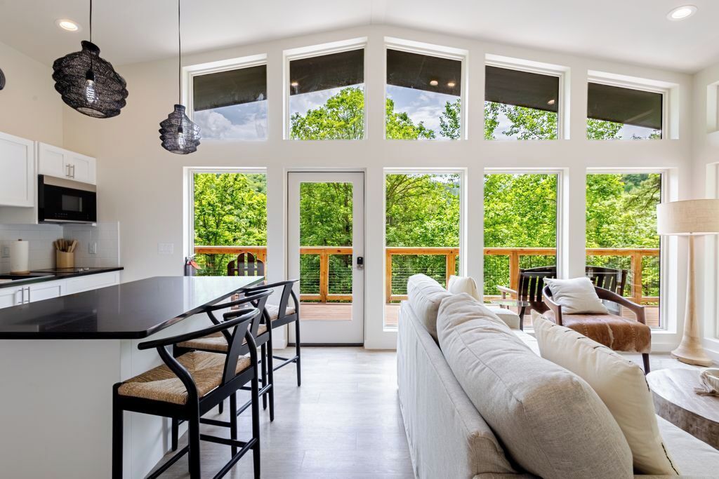 A modern kitchen with a central island, dining area with chairs, and a large window overlooking a deck.