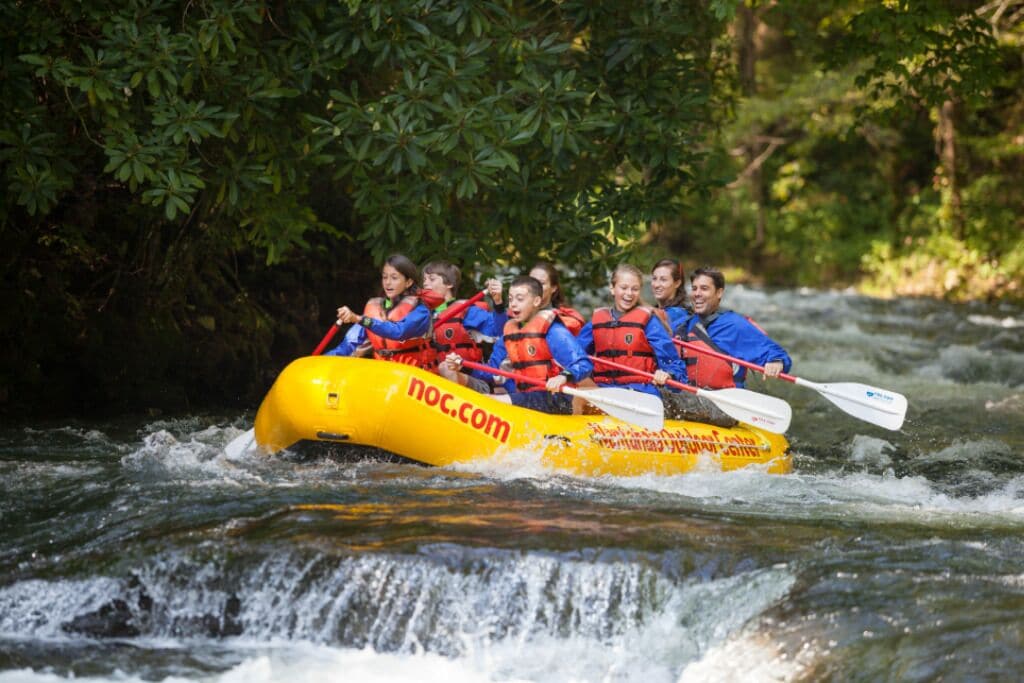 A group of people in a yellow raft with red life jackets navigating a river.