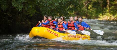 A group of people in a yellow raft with red life jackets navigating a river.