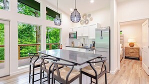 Una cocina moderna con una isla central, luces colgantes y grandes ventanales con vistas a un paisaje verde.