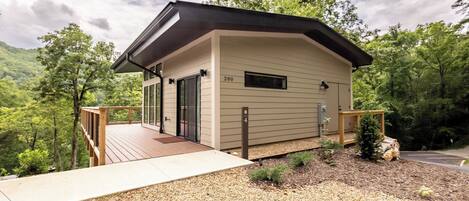 A modern cabin with a deck, surrounded by forest.