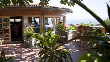 A building with a curved roof, large windows, and a patio area with wicker furniture and potted plants.