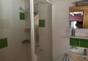 A bathroom with white tiles, a glass shower enclosure, a sink with a mirror, and a green-tiled accent wall. - Le Communal Chalet La Renarde (Val d'Illiez)