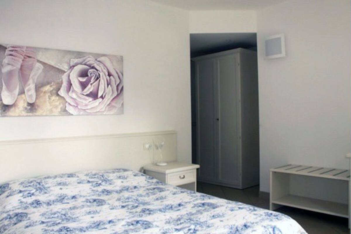 Ein Schlafzimmer mit Bett, Nachttisch, Kleiderschrank und einem Gemälde von Ballettschuhen und einer Rose an der Wand.