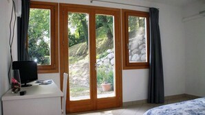 Une chambre à coucher avec un lit, un bureau équipé d’un ordinateur et une porte-fenêtre coulissante donnant sur un jardin.