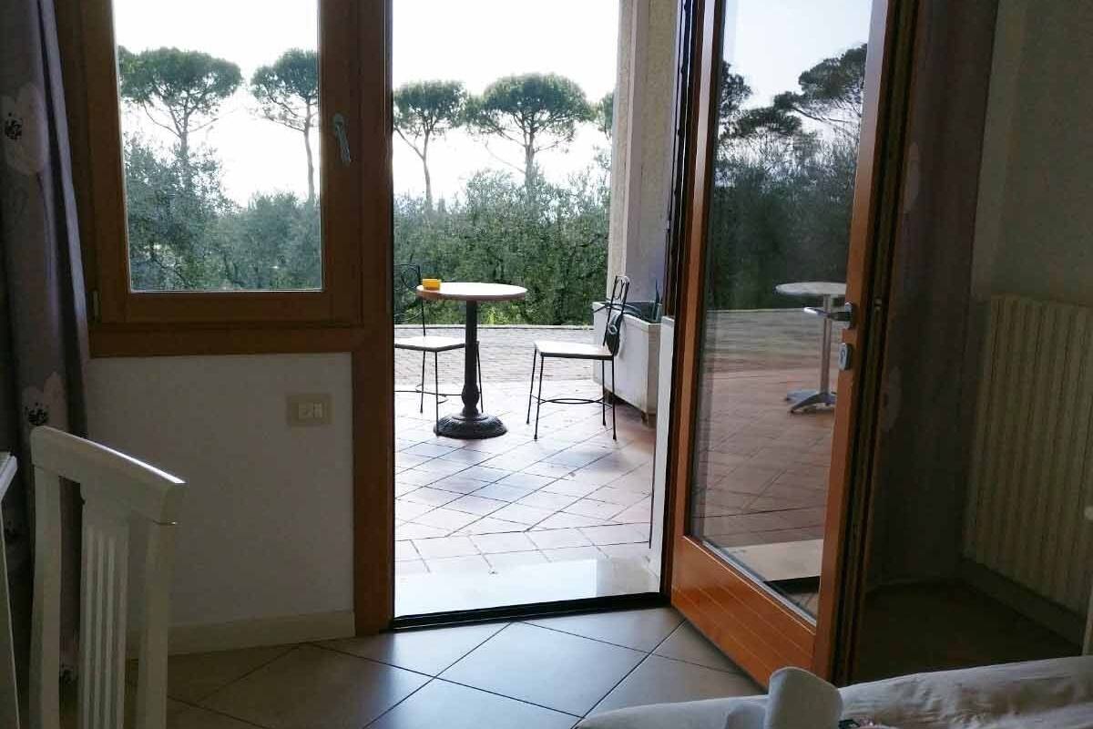 Ein Schlafzimmer mit Bett, Stuhl und Blick auf eine Terrasse mit Tisch und Stühlen.