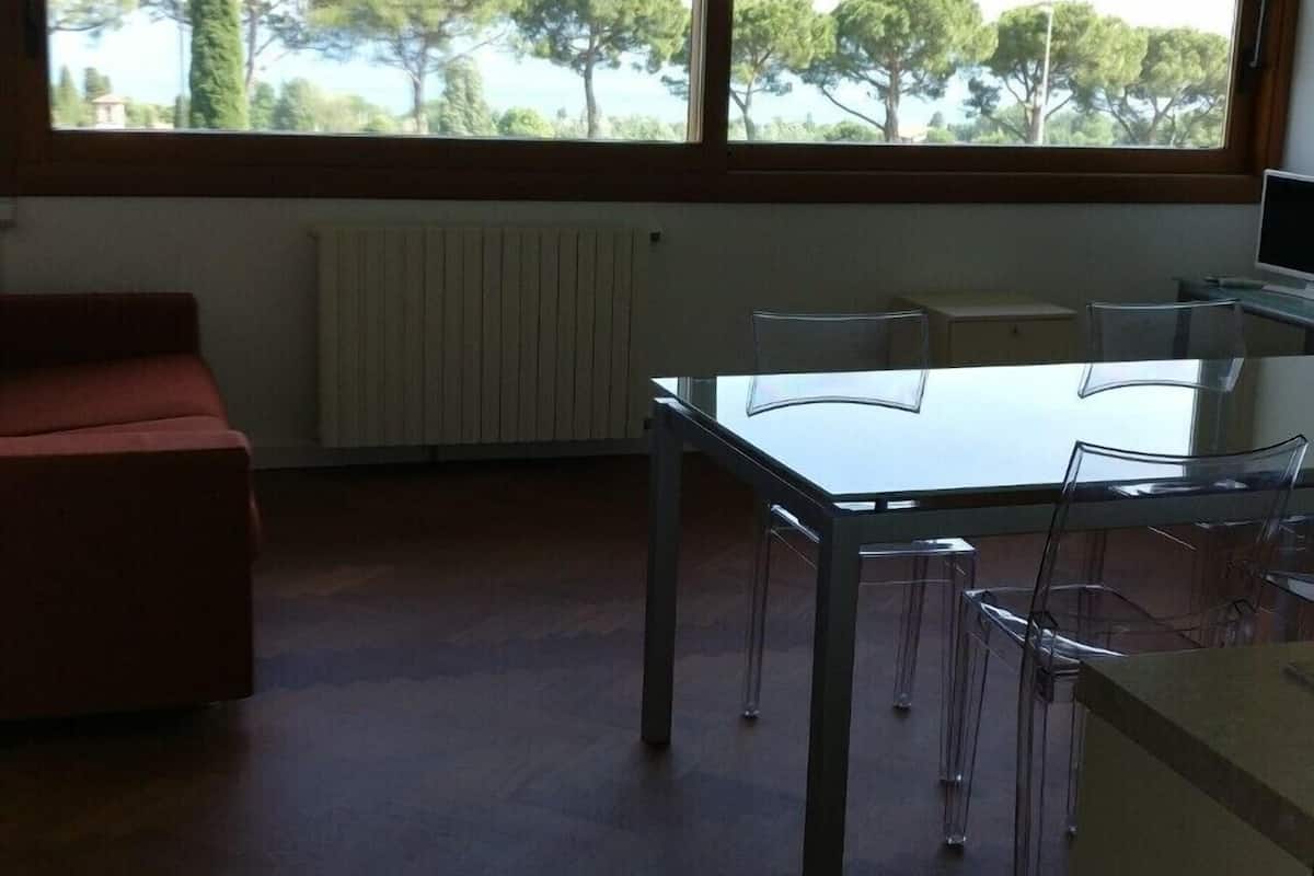 Ein Zimmer mit großem Fenster, einem Tisch mit Stühlen, einem Heizkörper und einem roten Sofa.