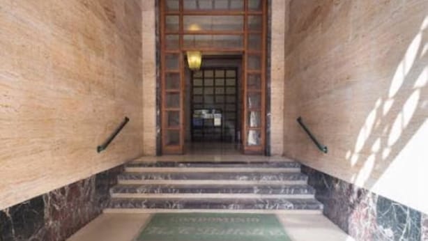A marble staircase leading to a door with a glass panel, a green mat with text, and a light fixture above the door. - Toledo one (Naples)