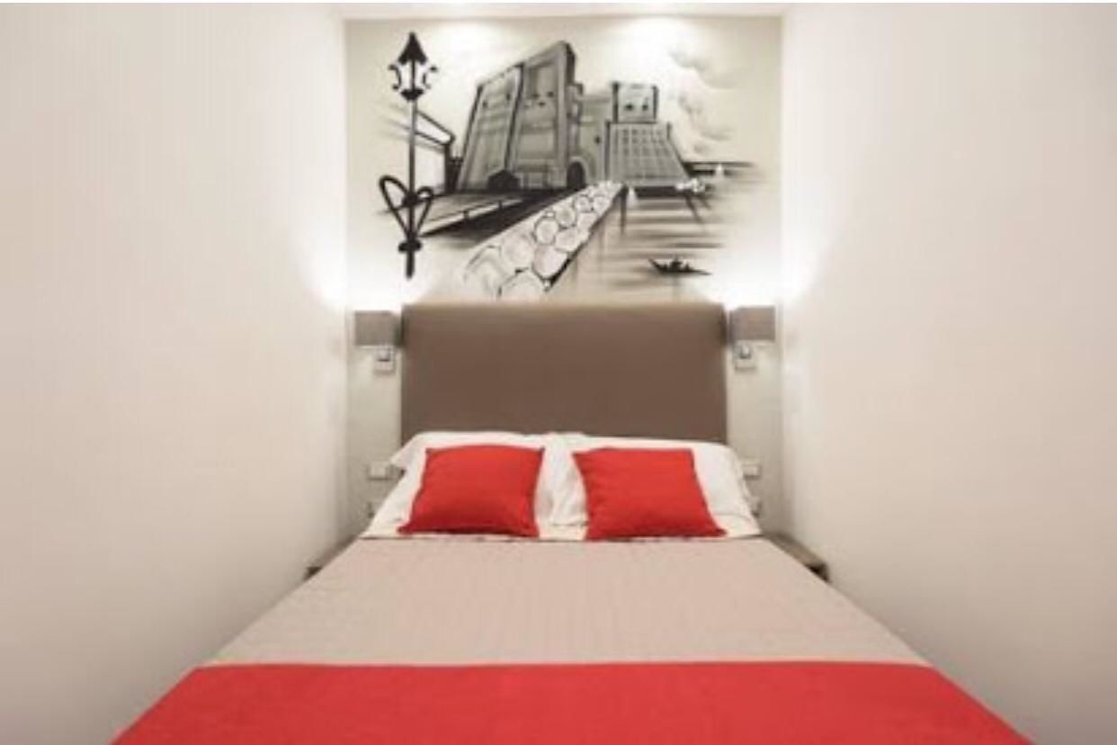 Habitación de hotel con cama, cabecera y pared con un mural en blanco y negro.