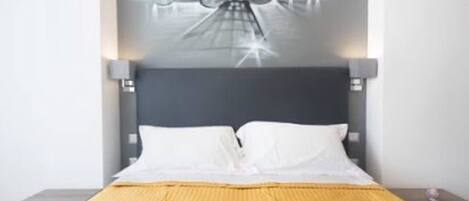 A modern hotel room with a large bed, a dark headboard, and a wall-mounted light fixture.