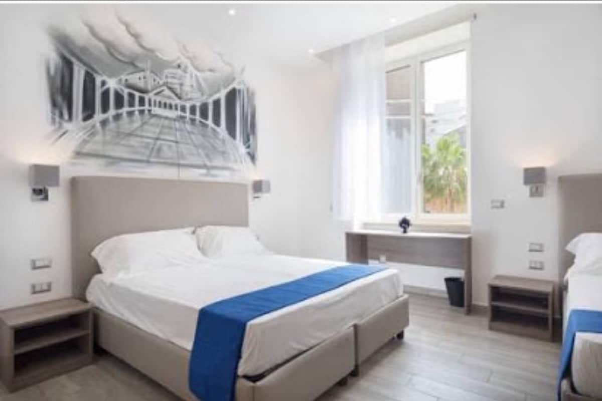 A modern hotel room with a large bed, a window with a view, and a unique wall art piece.
