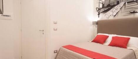 A hotel room with a bed, a door, and a wall-mounted artwork.