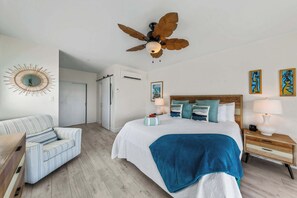 Ein Hotelzimmer mit Bett, Sessel, Nachttisch, Lampe und Deckenventilator.