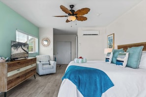 A bedroom with a bed, a chair, a television, and a ceiling fan.