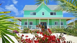 A two-story house with a green exterior, a front porch, and a staircase leading to the entrance.